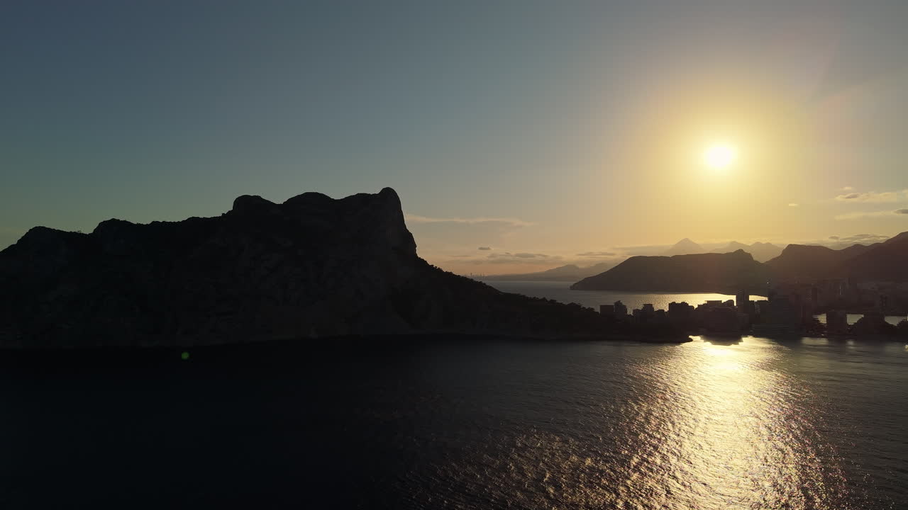 Gylden solnedgangsrefleksion på havvand med bjergsilhuet.