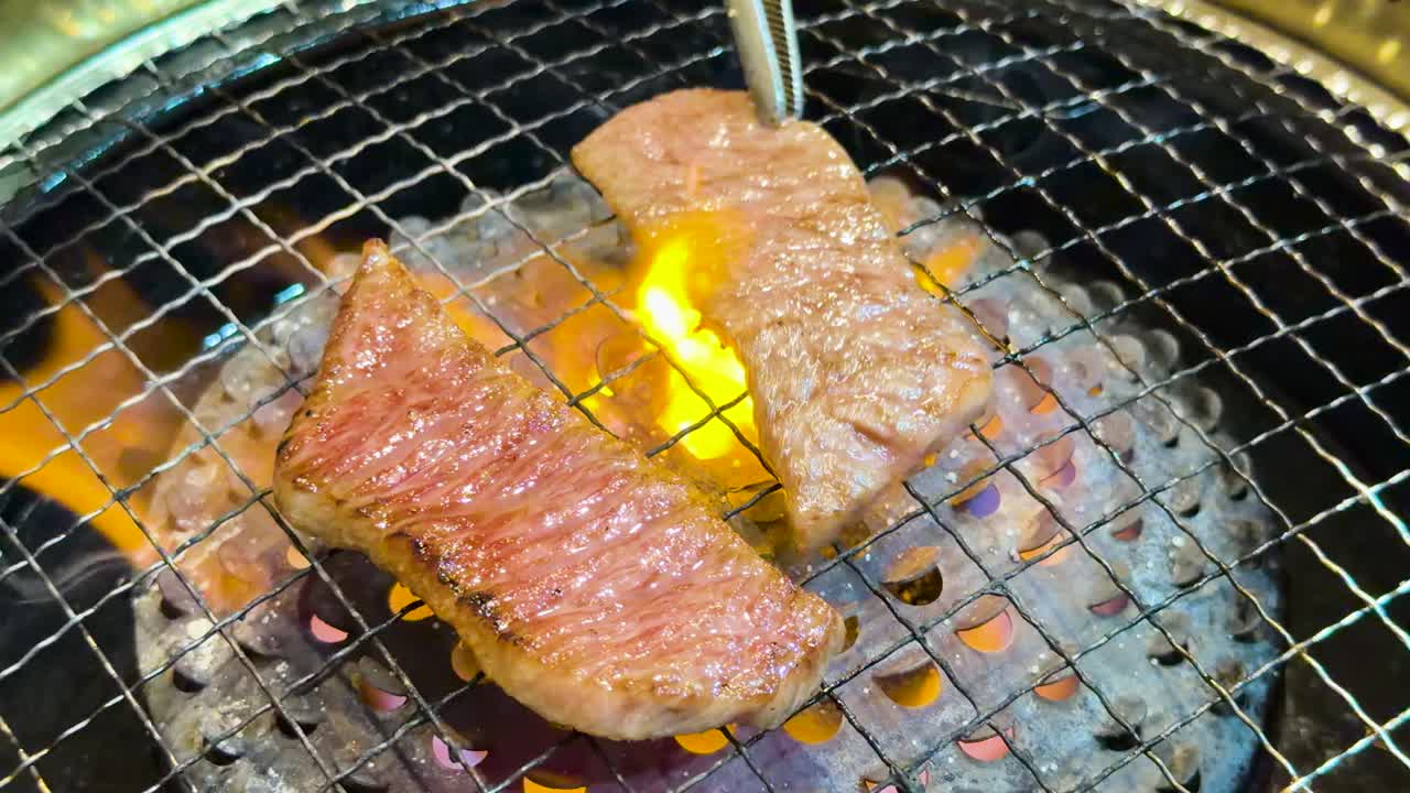 揺らめくオレンジ色の炎で網の上で焼ける霜降り牛肉のクローズアップ。