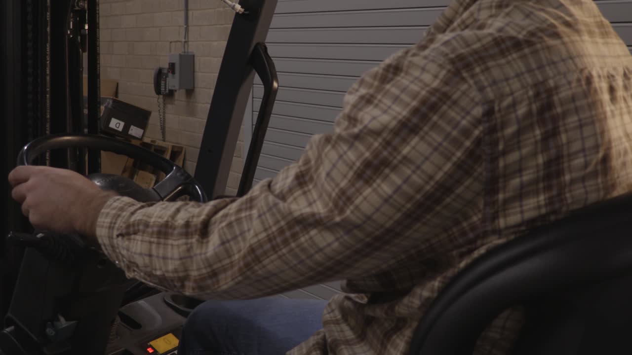 창고에서 지게차 레버를 조작하는 플란넬 셔츠를 입은 블루칼라 근로자