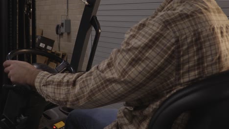 Blue-Collar-Worker-in-a-Flannel-Shirt-Operating-the-Levers-of-a-Forklift-in-a-Warehouse