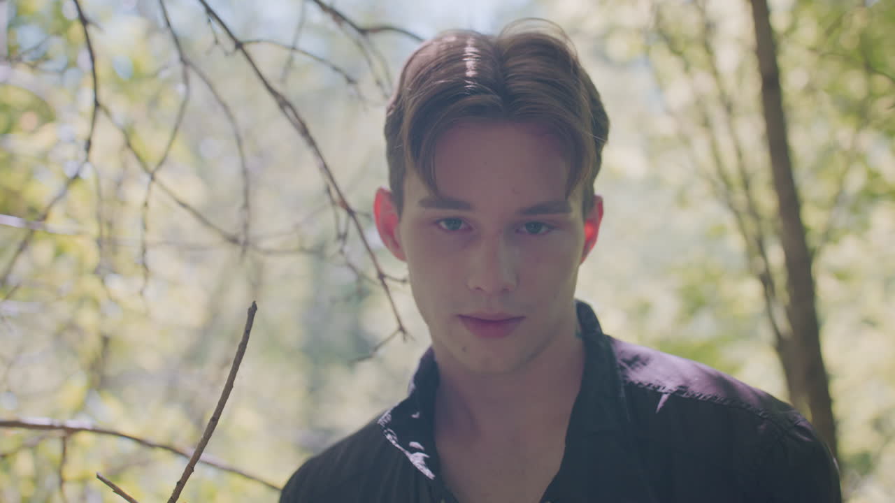 Close view of adventurer standing in sunlit forest, looking downward with intense expression while breathing deeply, appearing lost in thought during quiet moment of reflection and problem solving