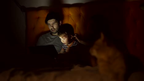 happy family with little son learning to play tablet computer lying in bed with cat at home