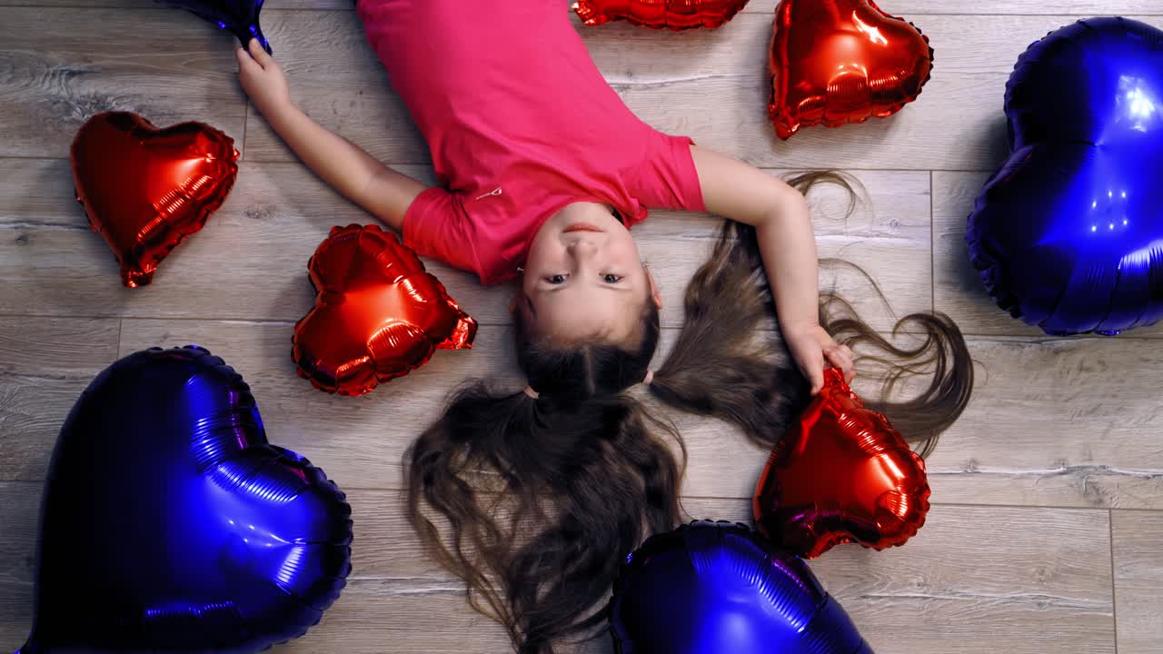 Cute girl lying on floor with balloons. Top creative view of little girl on floor with balloons in form of heartin