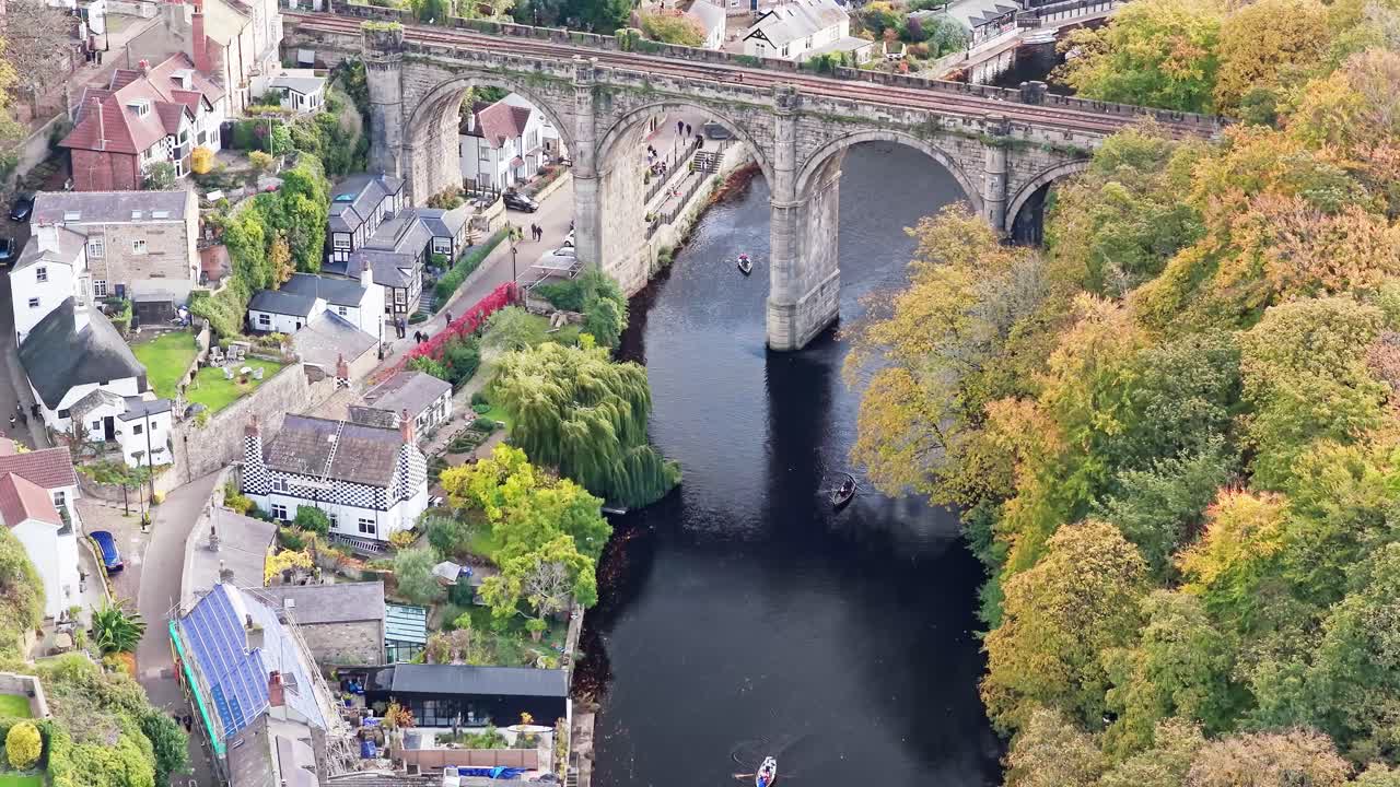 High angle aerial shot shows stone Knaresborough Viaduct carrying the Harrogate railway line over the River Nidd, flanked by boats, riverside houses, and historic buildings in Knaresborough, England