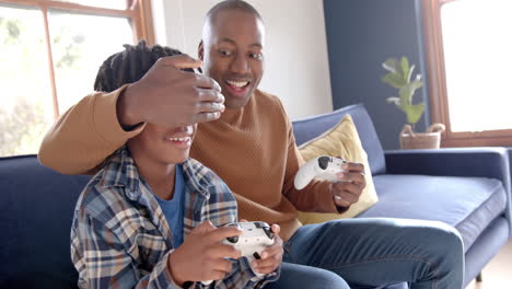 happy african american father and son playing video games and fooling around at home, slow motion