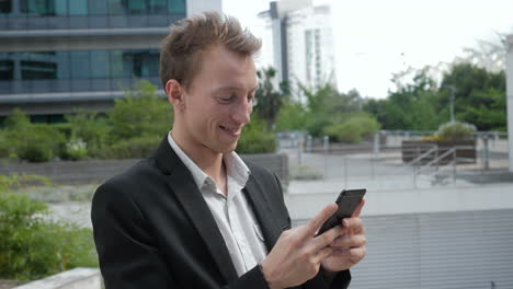 Young-Caucasian-man-texting-on-phone-outside,-smiling
