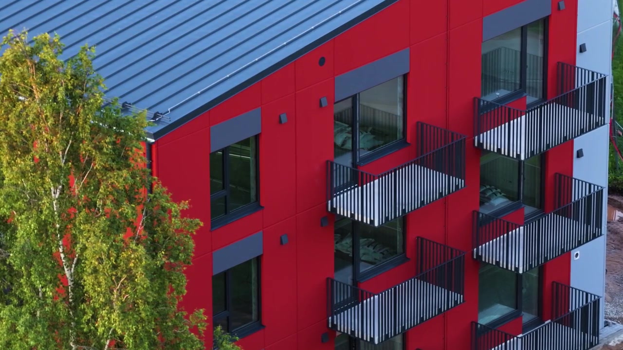Fachada de edifício de apartamentos vermelho recém-construído com varandas e árvores verdes próximas em vista aérea