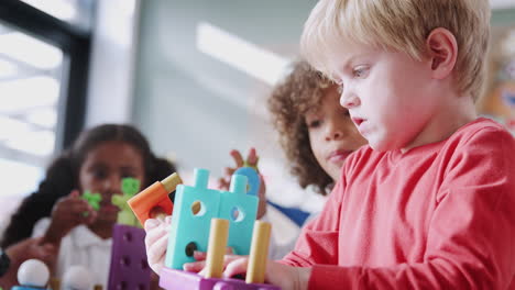 infant school boy using educational construction toys with his classmates, low angle, close up