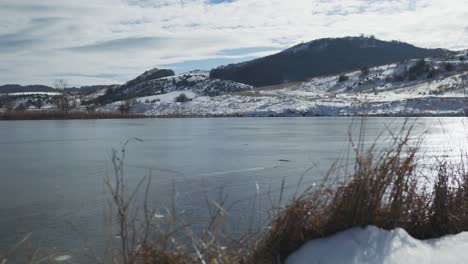 Winter-frozen-mountain-lake-snow-covered-sunny-cloudy-day-panning-left