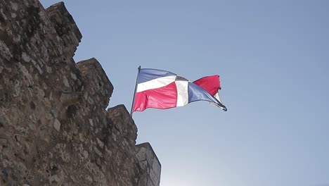 toma en cámara lenta de la bandera de la república dominicana volando alto con un sol radiante detrás y un cielo azul claro