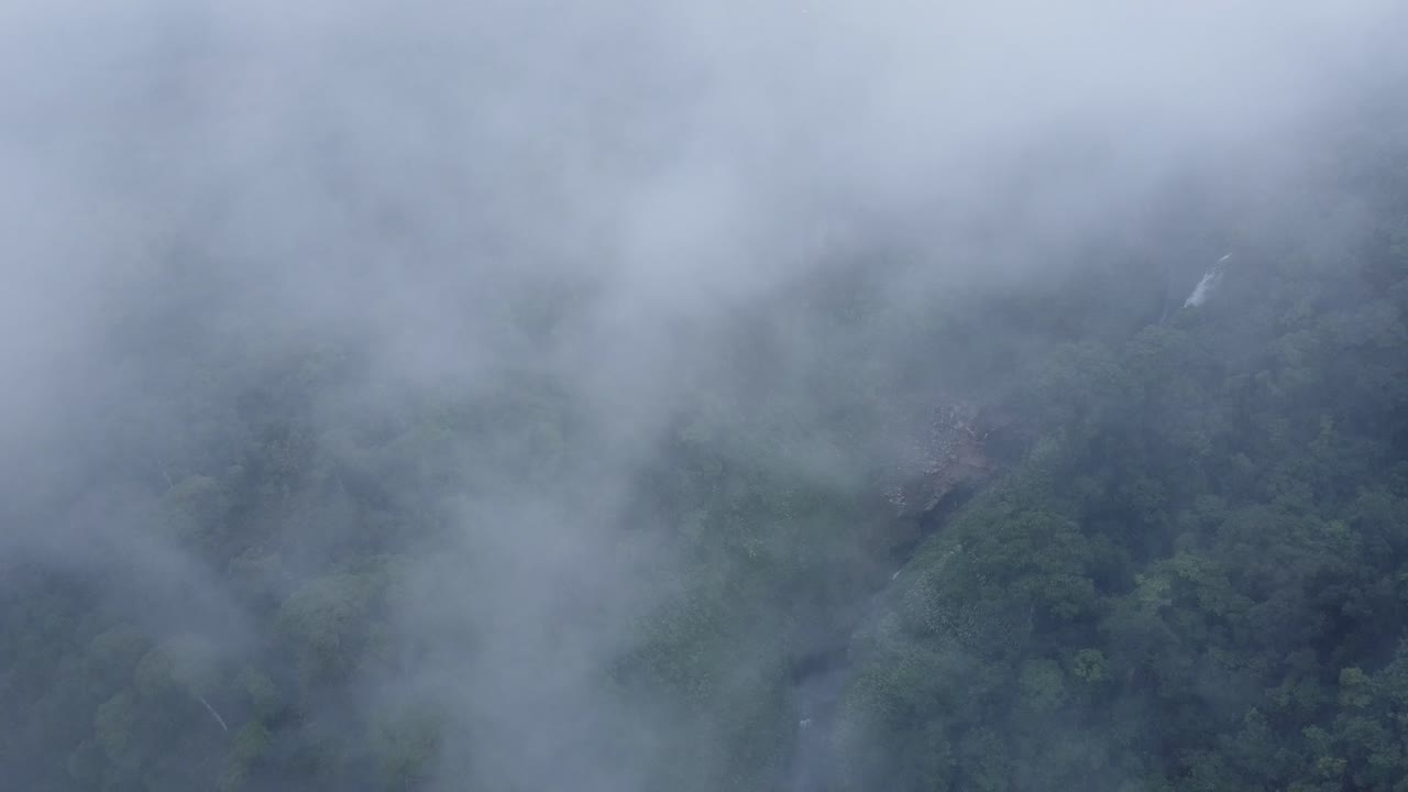 A breathtaking aerial drone shot captured from above a layer of clouds, providing a unique vantage point of Catarata del Toro in Costa Rica