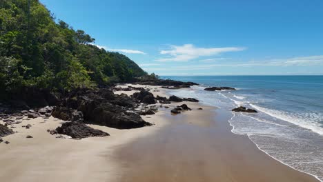 drone glides above a deserted tropical beach with rocky shoreline, lush rainforest, and turquoise water under bright midday sunlight. smooth, cinematic camera movement