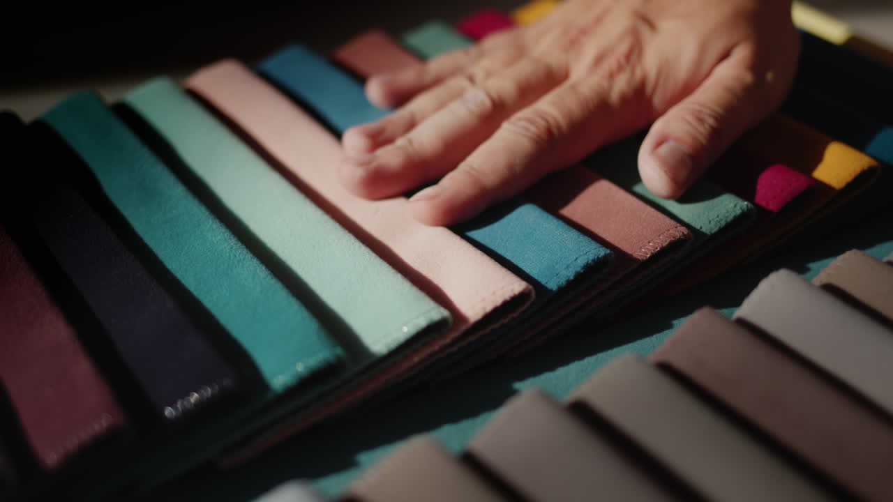 A man's hand touches samples of multi-colored fabric. Designer selects textiles for the project. Static shot
