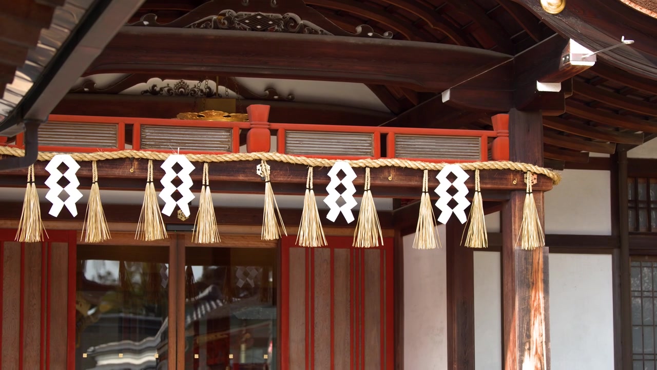 Static medium shot of sacred rope and paper streamers hanging from a wooden temple structure.