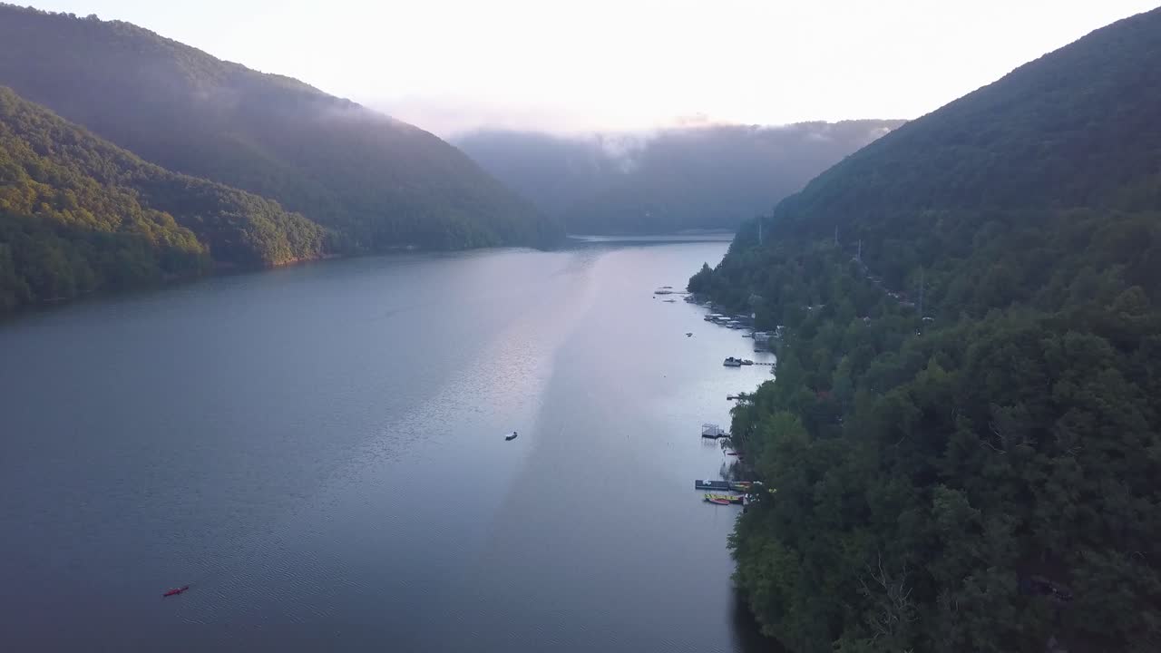 일출 때 루마니아의 타르니타 호수 해안선에 물 위에 보트가 있고 숲 속에 숨겨진 집 부두에 정박해 있습니다.