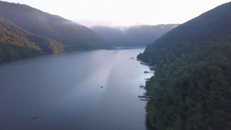 shoreline of tarnita lake in romania at sunrise with boats on water and moored at docks of homes hidden in forest