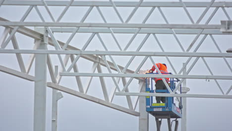 a worker welds a steel frame for a construction from an aerial work platform