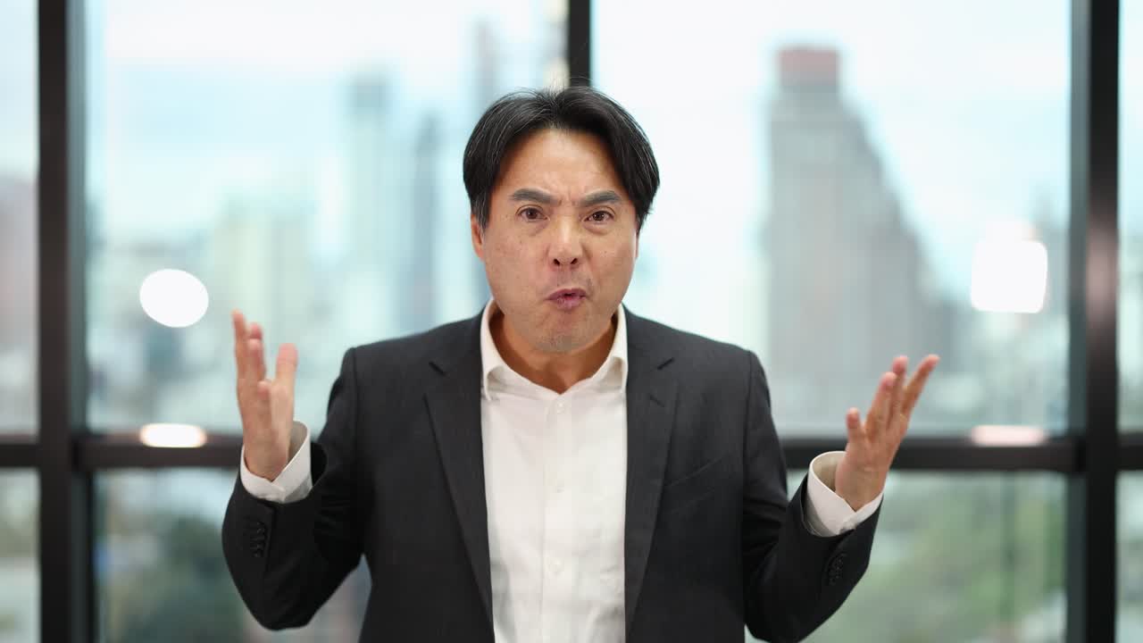 Asian businessman in suit expresses frustration with open hands, bright office, steady camera, natural light