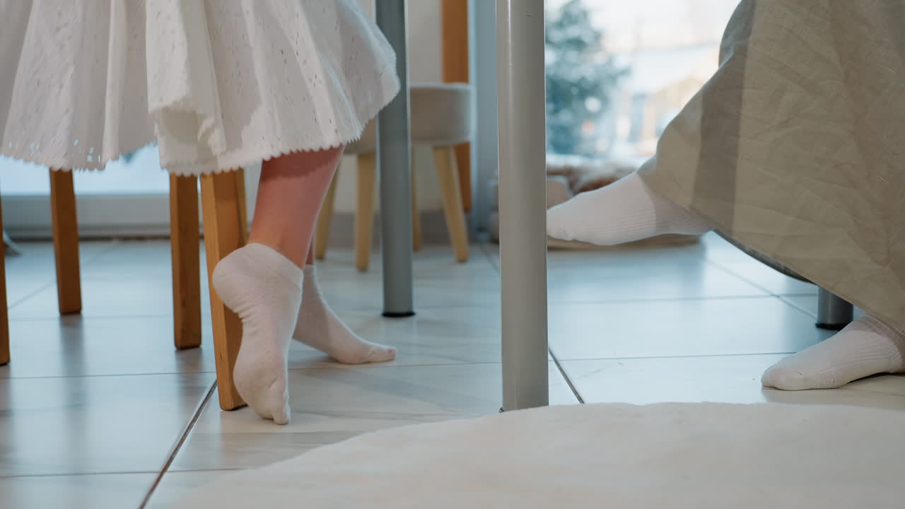 Leg view of three people walking and sitting down on chairs, all wearing white socks, the image captures the cozy atmosphere of a family room with a clean white tiled floor