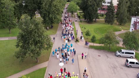 a ceremonial procession of people moves through the streets of limbaži, with participants walking along the cobbled roads. the event creates a festive and community-focused atmosphere in the city.