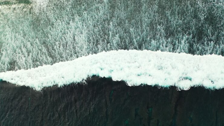 Beautiful white waves of deep dark ocean splashing and foaming on exotic beach, sea texture seen from above, copy space