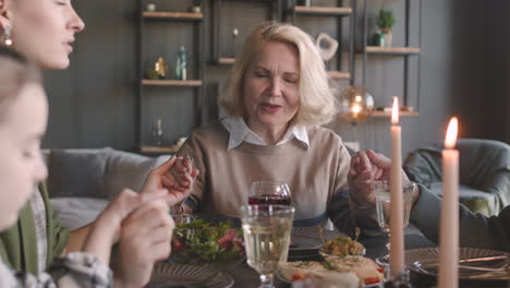 senior woman sitting at dinner table and praying before meal with her family at home 1