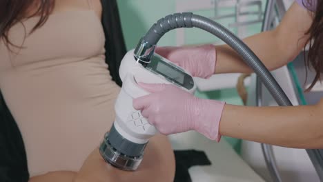 a beauty expert is utilizing a firming and anti-cellulite device on a woman's legs in a beauty salon - close up