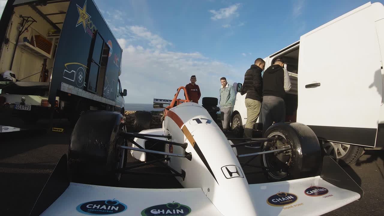 Men Walking Closed To A White Racing Car Parked Between A Van And A Truck At The Roadside On The Hill In Malta - GoPro Pan Shot