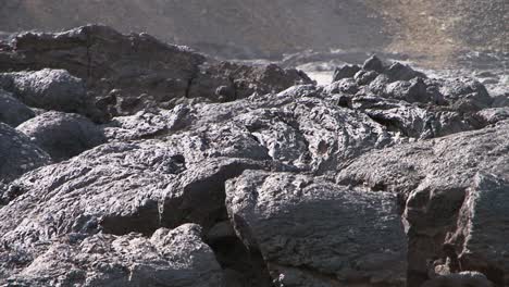 detail of solidified lava with some steam rising, slope of a hill in background