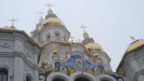 a low-angle view of the golden domes and a religious mosaic on the church of the holy myrrh-bearing women in kharkiv, ukraine. a detail of the city's architecture on a foggy day