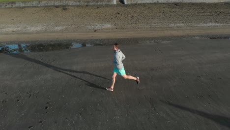 Toma-Aérea-De-Un-Joven-Trotando-En-Una-Playa-En-Auckland,-Nueva-Zelanda