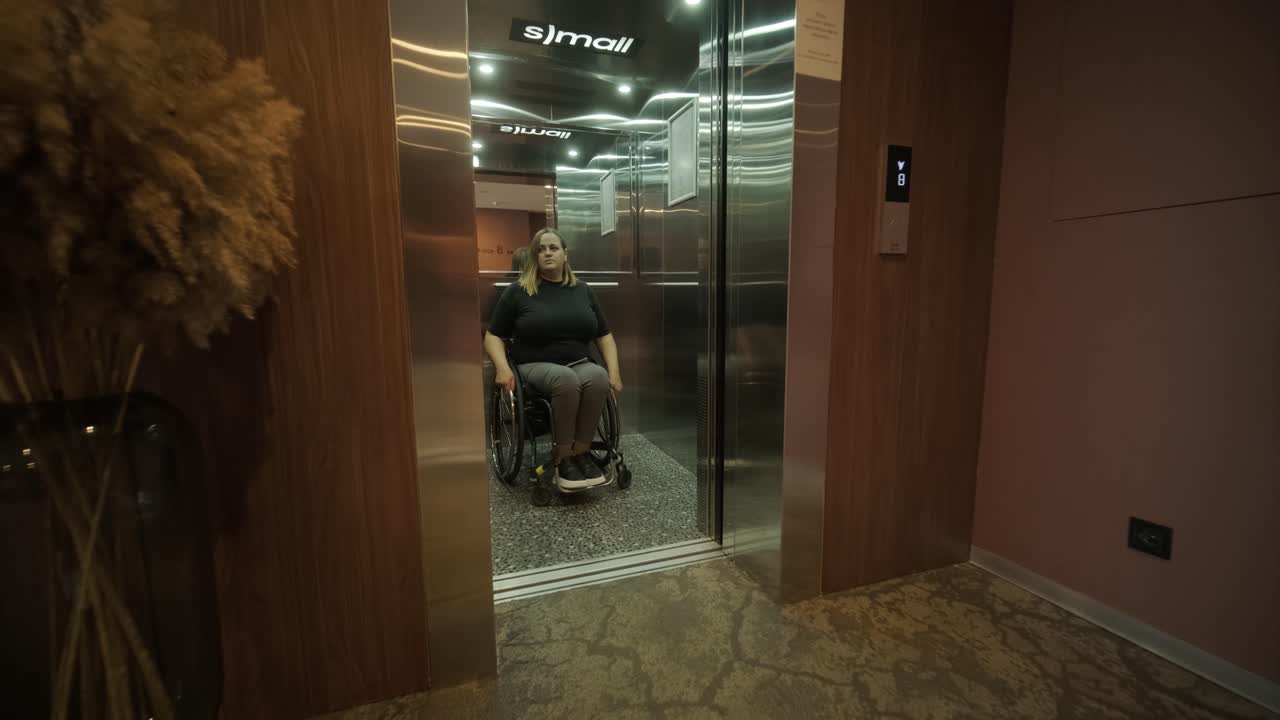 A woman in a wheelchair approaches an elevator in a hotel lobby, showcasing accessible accommodations and modern design. The scene emphasizes mobility, independence, and inclusivity in hospitality.
