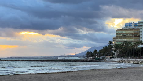 marbella beach on a windy cloudy day with palm trees, apartments and mountains in spain, interesting sunset sky, 4k shot
