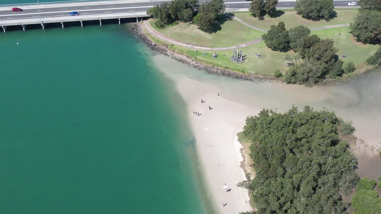 친구들이 모여서 풍랑 호수 (illawarra) 의 다리 근처의 모래 해변을 따라 산책합니다.