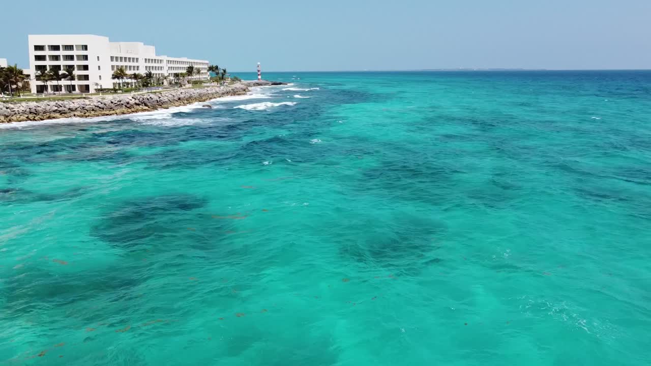 Drone aereo che vola sopra l'acqua turchese dell'oceano di Cancun con un faro sullo sfondo, Messico