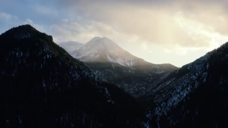 static aerial drone shot of a winter landscape of mount timpanogos in the background surrounded by a pine tree forest during sunset from the frozen tibble fork reservoir in american fork canyon, utah