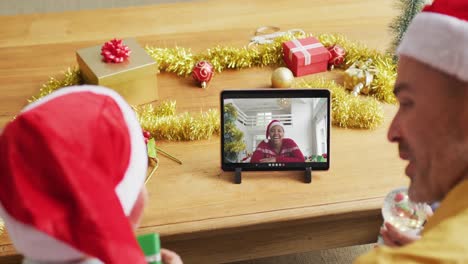 Padre-E-Hijo-Caucásicos-Con-Gorros-De-Papá-Noel-Usando-Una-Tableta-Para-Una-Videollamada-Navideña-Con-Una-Mujer-En-La-Pantalla