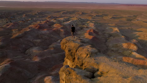 hombre en el borde de un acantilado en tsagaan suvarga en el desierto de gobi de mongolia al atardecer - retiro de drones