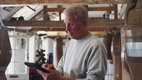 senior male boxing coach in gym tracking training using digital tablet