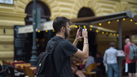 male tourist rises phone to take pictures of budapest with blurred background