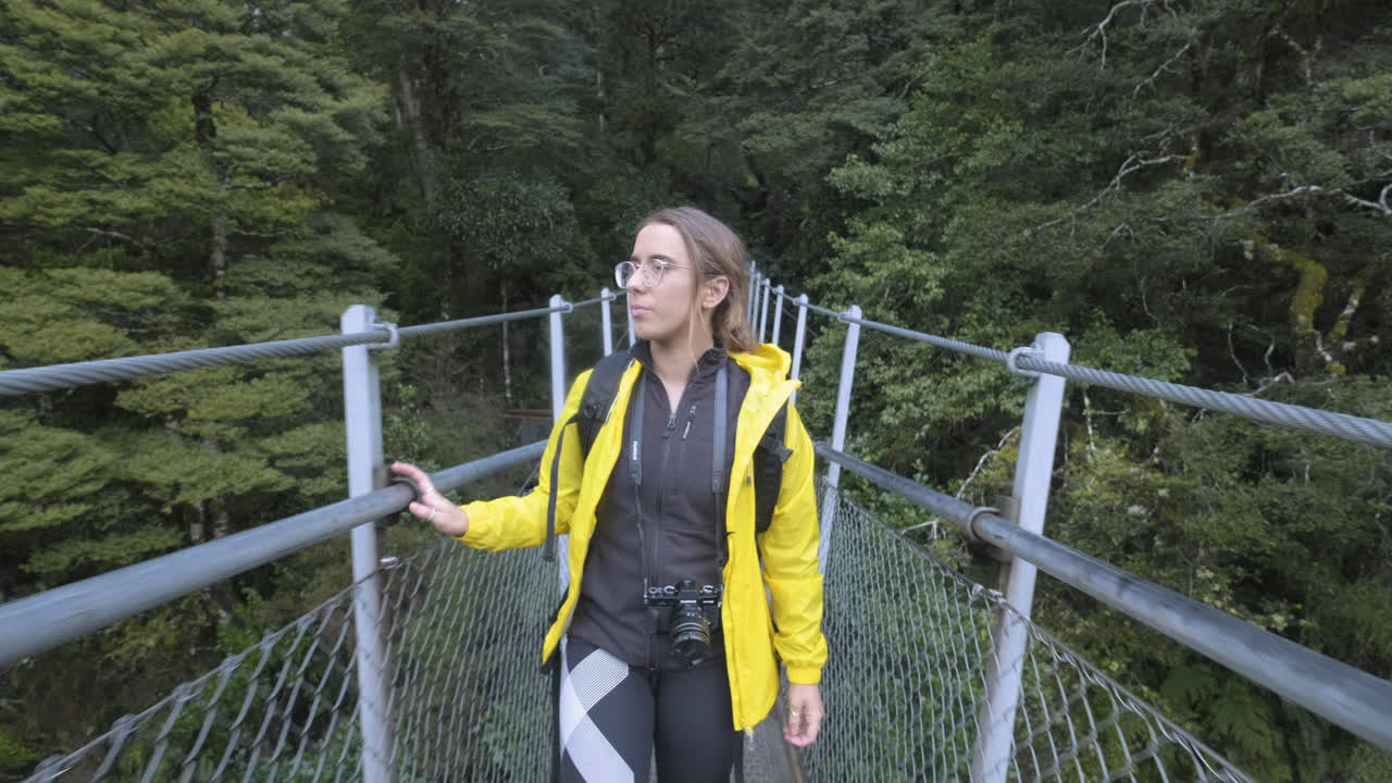 Ragazza con giacca gialla e fotocamera che cammina lungo un ponte in Nuova Zelanda