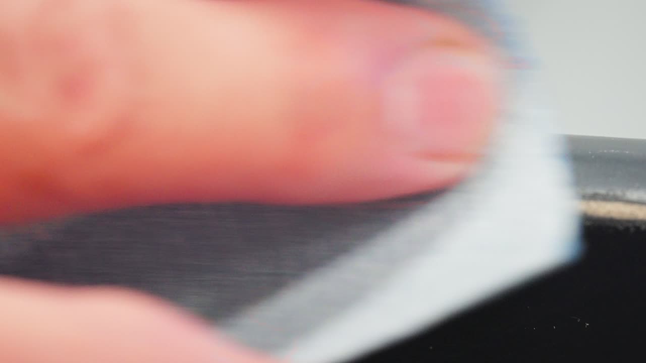 Slow motion close up shows hand sanding chair edge, grey paint coming off