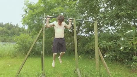 young fit man doing behind-neck pullups outdoors surrounded by nature