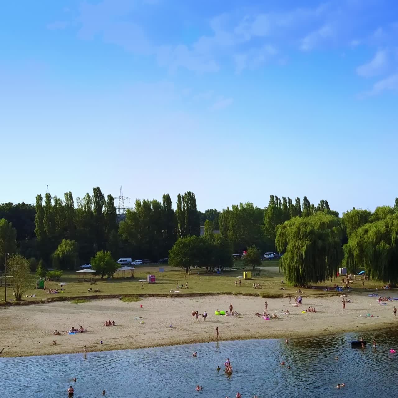 Approaching the bank of the river from water. People resting on the beach and swimming in the water. Sunny day footage