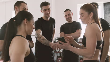 strong young woman shows something to her gym buddies on her mobile phone