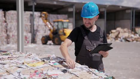 un trabajador de una planta de reciclaje usa una tableta mientras inspecciona un fardo de papel.