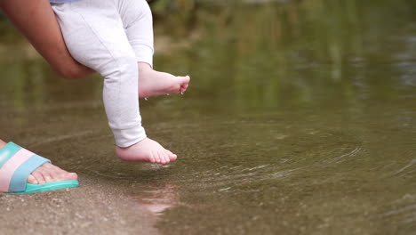 tiny baby feet trying water in the pond. mom's hands holding a baby close to the river and kid deeps them into water.