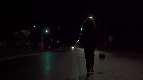 teenage girl in black sweater dribbling basketball down the yellow line of a wet city street at night with headlights in distance