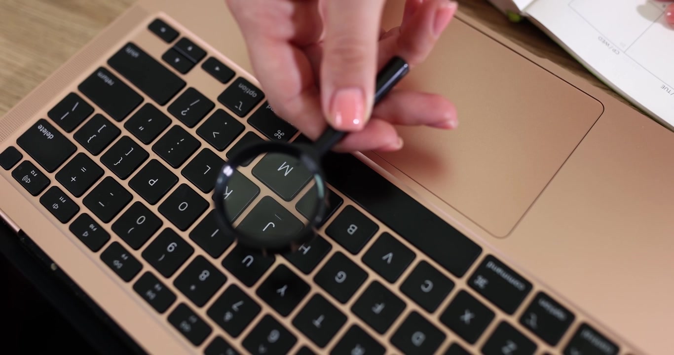 Fingers with a magnifying glass above the keyboard closeup