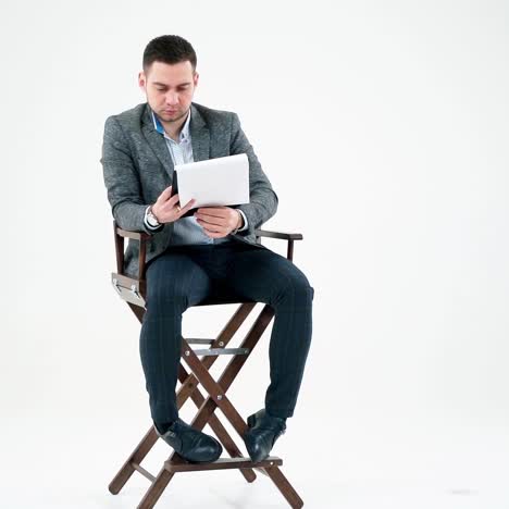 handsome businessman reading documents. young man in grey suit sitting on a wooden chair and looking the paperworks on white background.